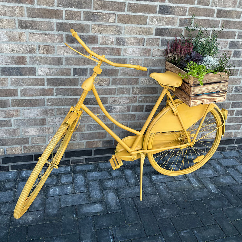 gelb angesprühtes Fahrrad mit einem Korb mit Blumen auf dem Hinterrad