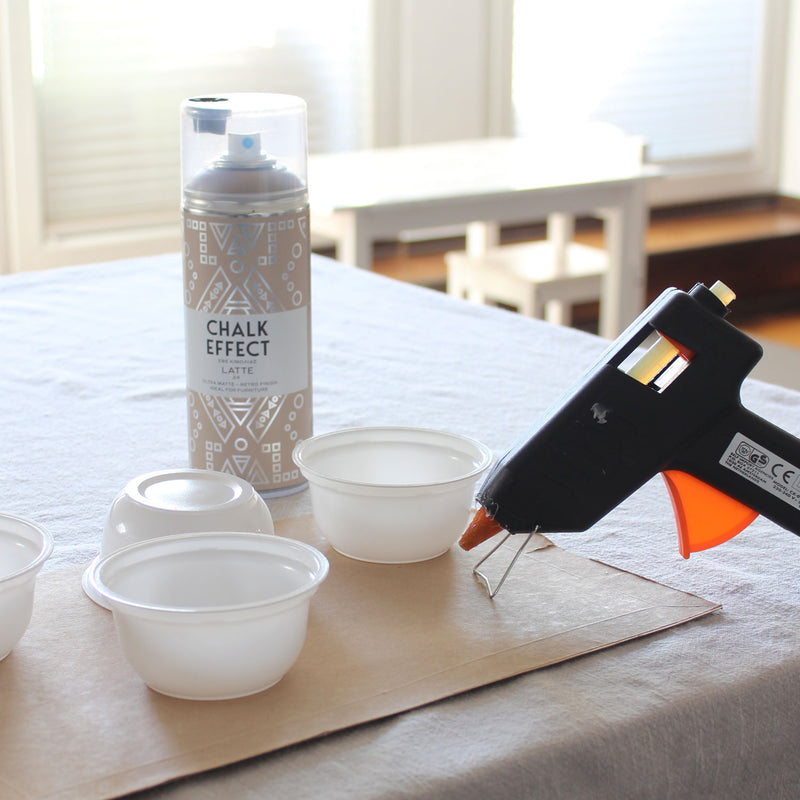 leere Joghurtbecher auf einem Tisch neben einer Heißklebepistole und einer CHALK EFFECT Spraydose