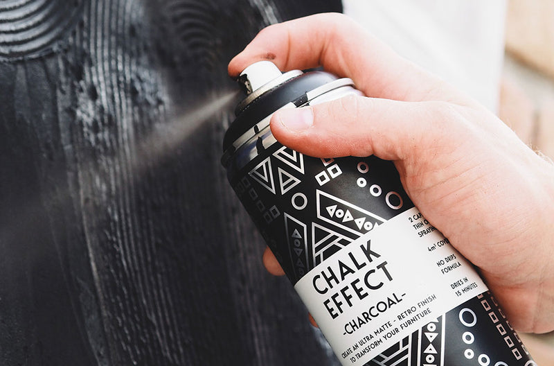 Hand, die mit der Farbsprühdose Cosmos Lac Chalk Effect Charcoal Holz besprüht