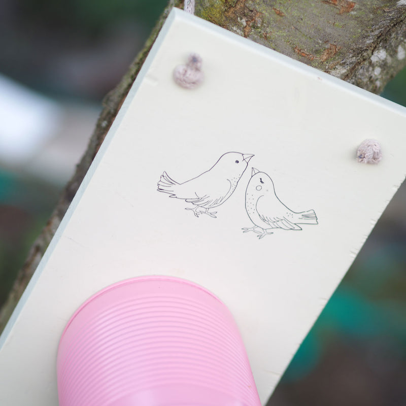 Holzbrett an Baum mit Zeichnung von einem Vogelpaar